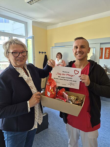 Einrichtungsleiterin Astrid Schneider übergibt den Präsentkorb an eine Pflegekraft. Im Korb sind verschiedene Süßigkeiten sowie eine Dankeskarte. 