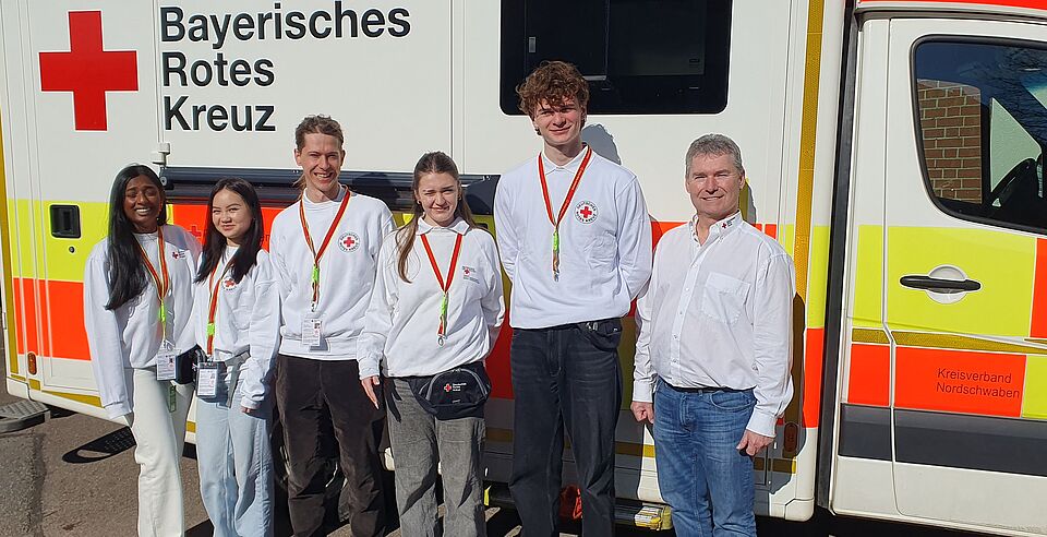 Das Bild zeigt BRK-Dienststellenleiter Joachim Regler (rechts), wie er zusammen mit den Werberinnen und Werbern vor einem BRK-Rettungswagen steht. 