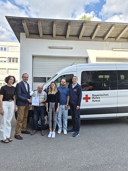 Das Bild zeigt von links nach rechts vor einem Fahrzeug des Fahrdienstes stehend Nicole Uhl (BRK-Fahrdienst), Johann Natzer (BRK-Kreisvorsitzender), Norbert Schuster (Sachgebietsleiter BRK-Fahrdienst), Viviana Popolo (BRK-Fahrdienst), Viktor Nau (BRK-Fahrdienst), Arthur Lettenbauer (BRK-Kreisgeschäftsführer). Herr Natzer übergibt das Zertifikat an Herrn Schuster. 