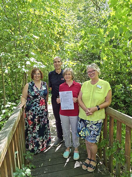 Auf dem Bild sind auf einer Brücke im Grünen von links nach rechts zu sehen: Diana Bader (PDL Tagespflege), Arthur Lettenbauer (Kreisgeschäftsführer), Sabine Hihler, Astrid Schneider (Einrichtungsleitung)