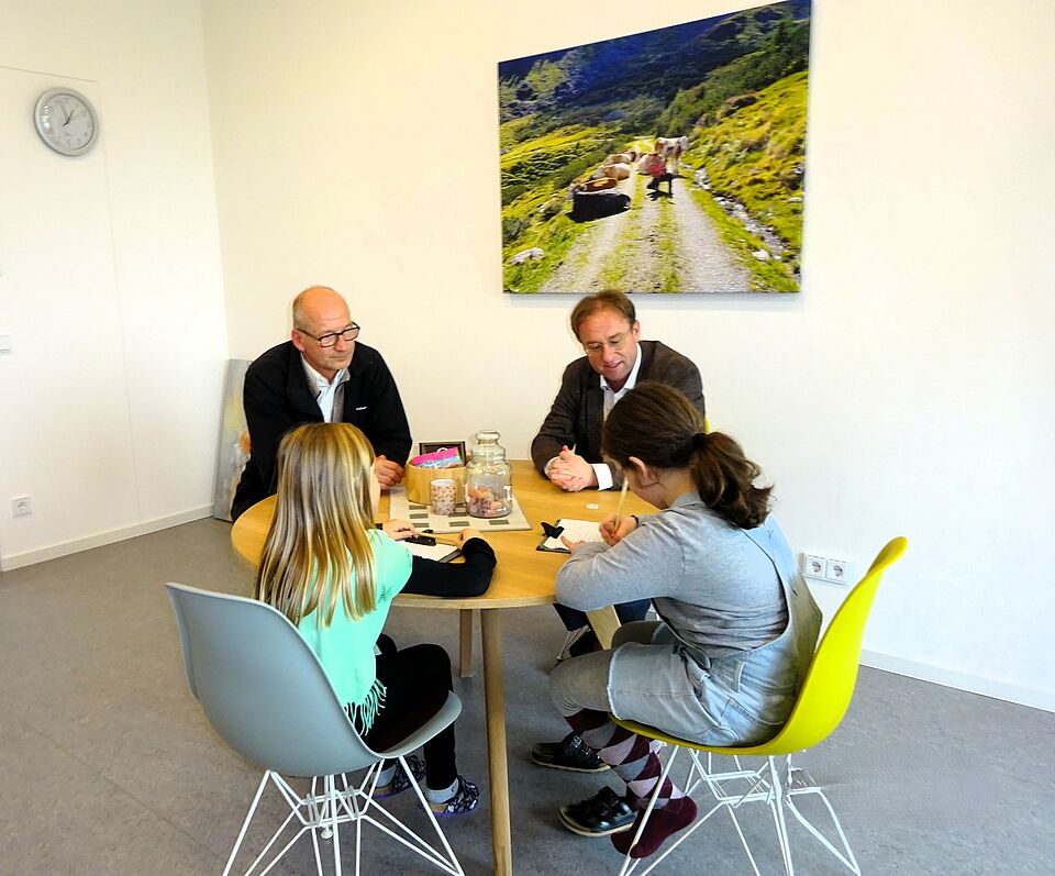Das Bild zeigt Martin Heilingbrunner und Wolfgang Fackler, die mit zwei Schülerinnen an einem runden Tisch sitzen und für die Schülerzeitung interviewt werden. 