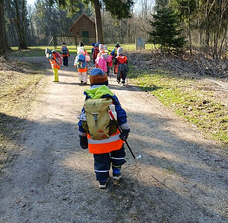 Die Kinder des Waldkindergartens "Lechfasane" laufen auf einem Waldweg und sammeln Müll ein. 