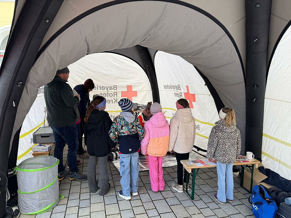 Das Bild zeigt Kinder, die sich das Behandlungszelt der SEG Betreuung am Nördlinger Frühjahrsmarkt ansehen. 